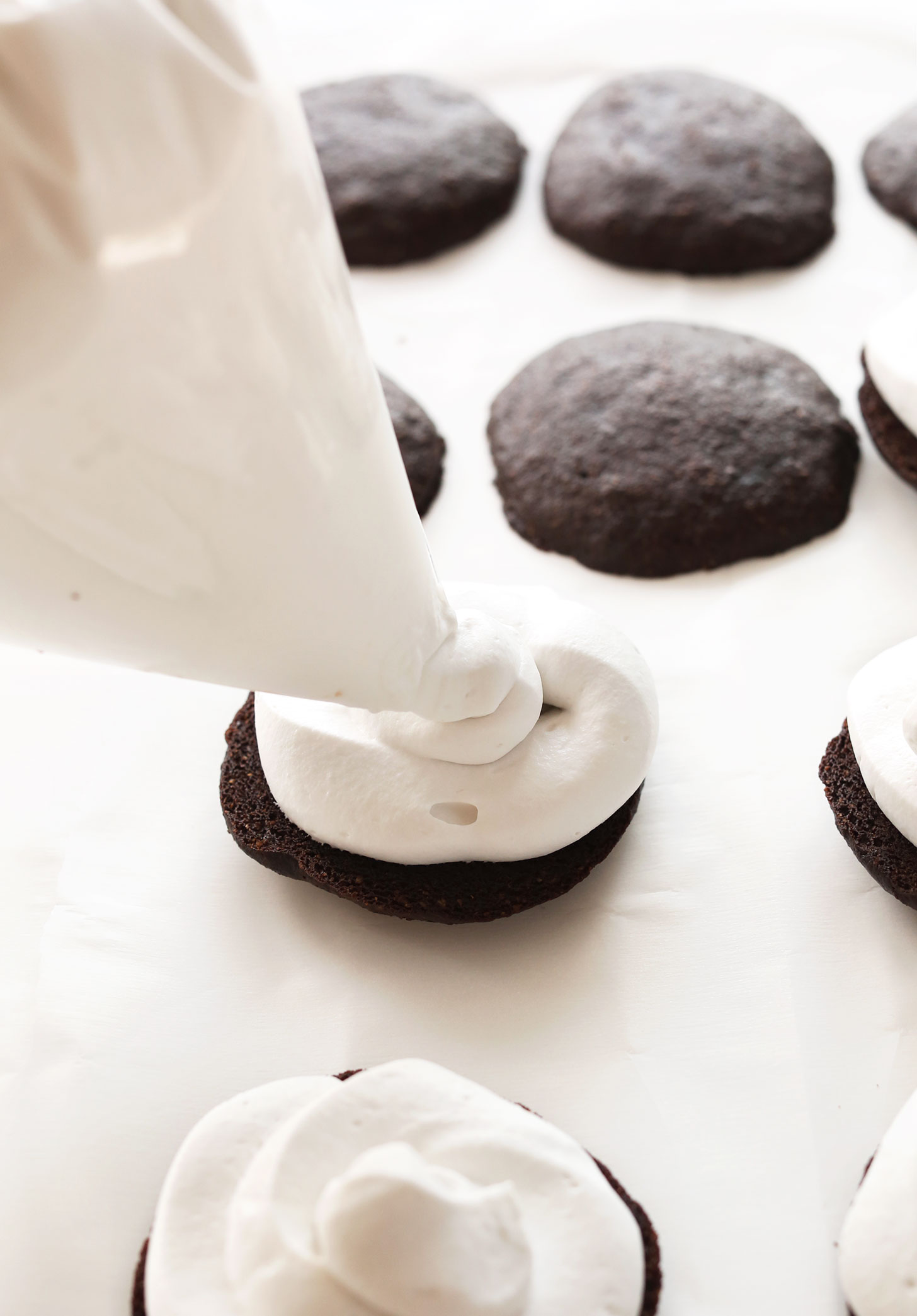 Using a pastry bag to swirl coconut whipped cream onto vegan whoopie pies