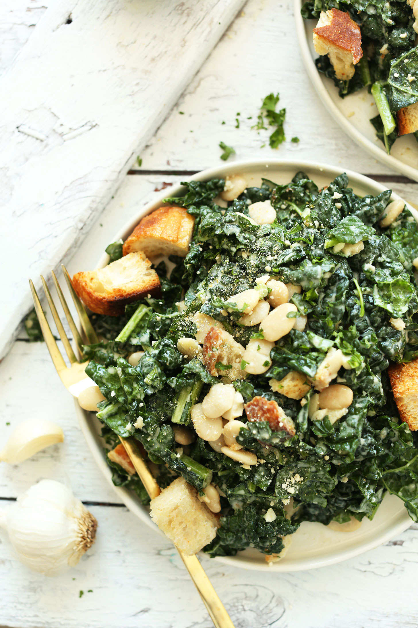 Dinner plate filled with Lemony Garlic Kale Salad with Butter Beans and Garlic Croutons