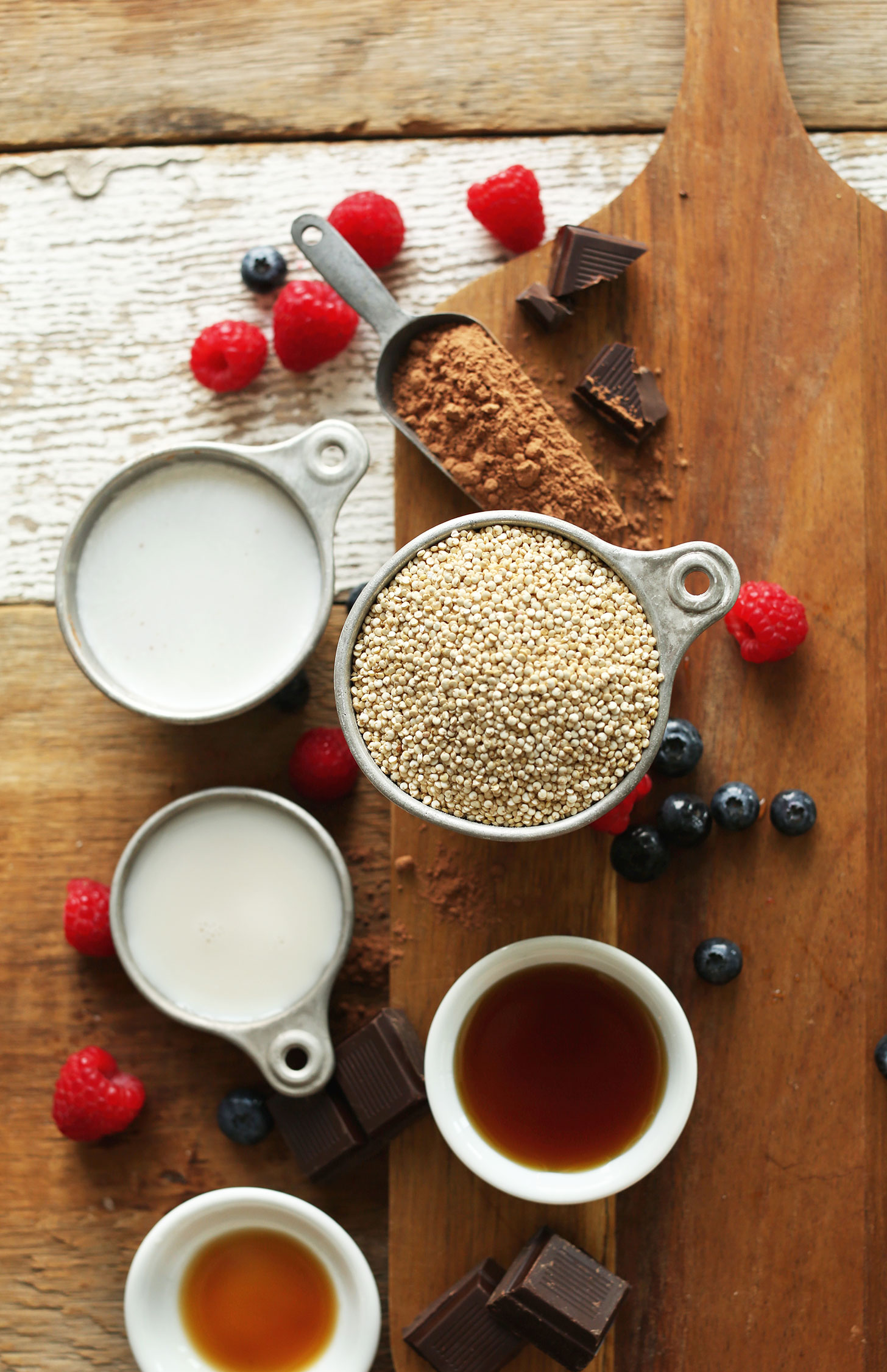 Cutting board with quinoa, cocoa powder, vanilla, almond milk, coconut milk, and maple syrup for making a delicious vegan breakfast