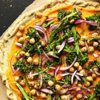 Cutting board with Butternut Squash Veggie Pizza made with chickpeas and broccolini