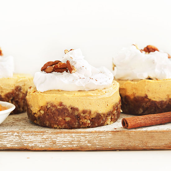 Wood board with three Vegan Pumpkin Cheesecakes topped with coconut whip and pecans
