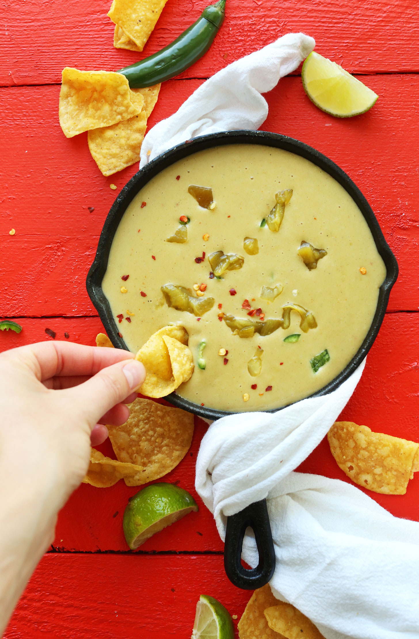 Scooping up Vegan Green Chili Queso onto a tortilla chip for a perfect plant-based snack