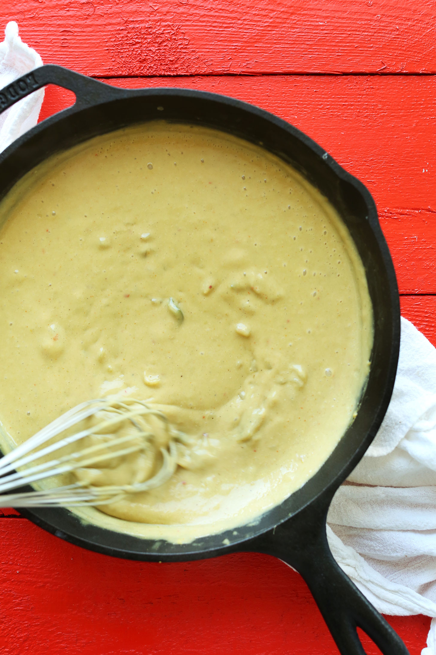 Whisking Vegan Green Chili Queso in a cast-iron skillet for a delicious vegan dip recipe