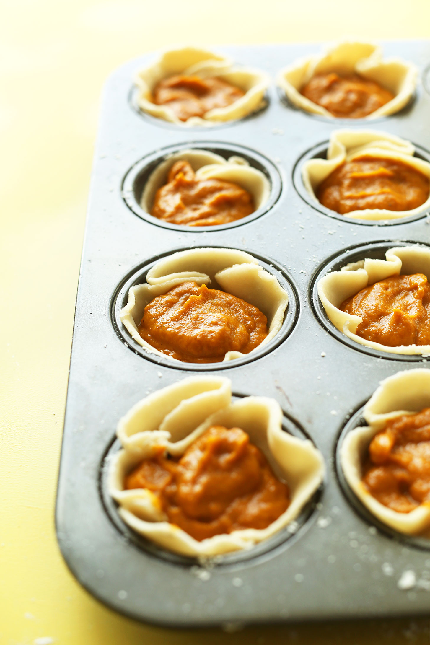 Muffin tin filled with Coconut Oil Crust and pumpkin pie filling for Mini Vegan Pumpkin Pies