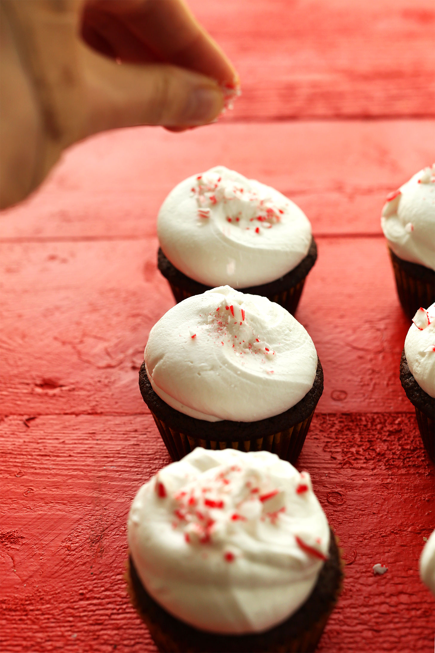 Sprinkling crushed candy cane onto cupcakes for a festive holiday dessert