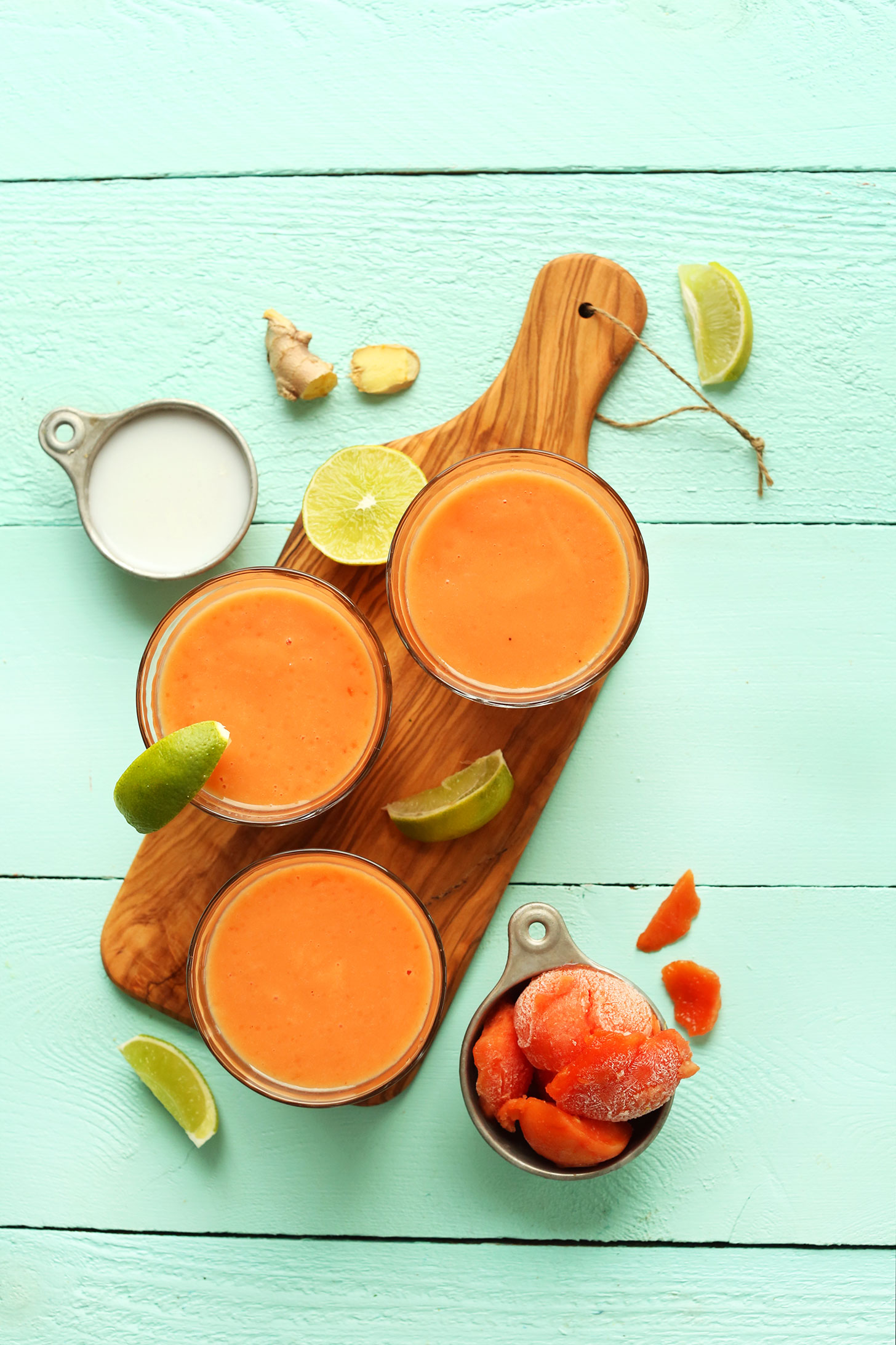 Wood cutting board with glasses of our bright and creamy vegan Papaya Detox Smoothie