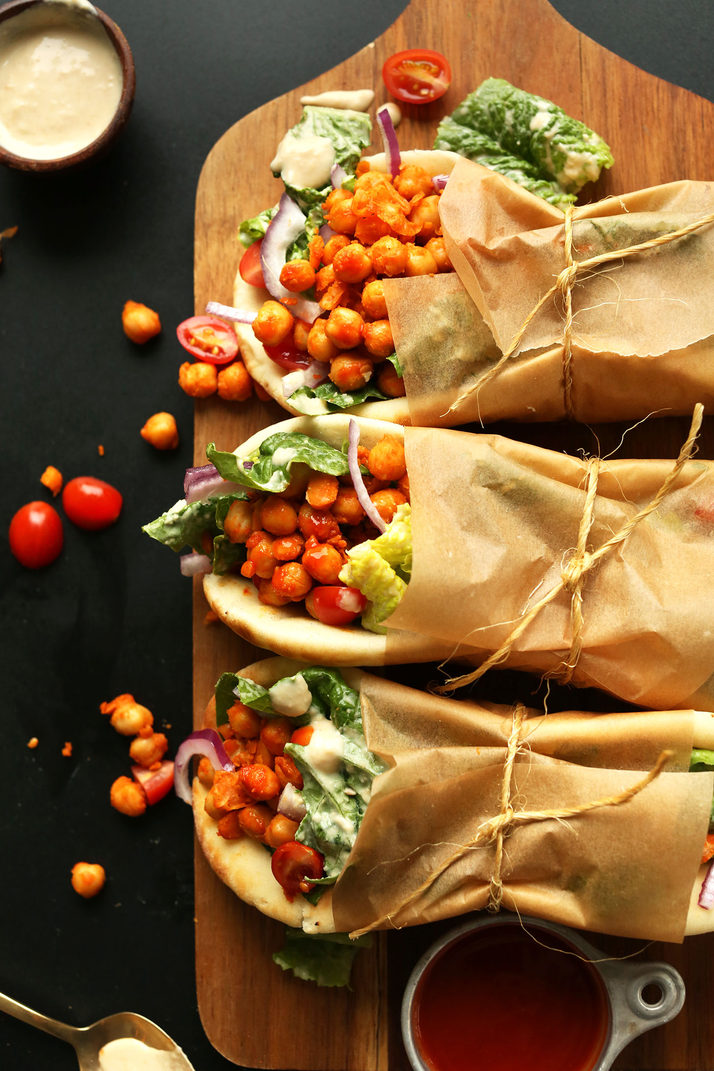 Wood board of Buffalo Chickpea Wraps rolled in parchment paper and tied with twine