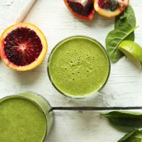 Two glasses filled with our Blood Orange Green Smoothie recipe alongside ingredients used to make it