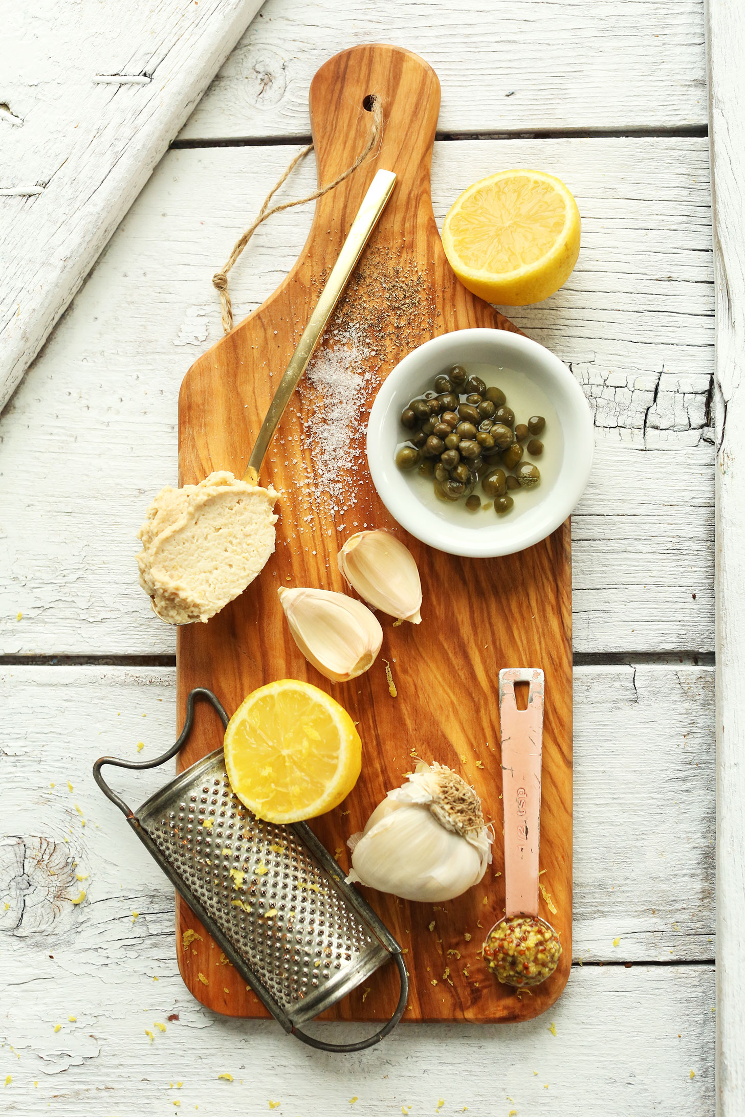 Wood board with capers, garlic, hummus, lemon juice, and spices for making simple vegan Caesar dressing