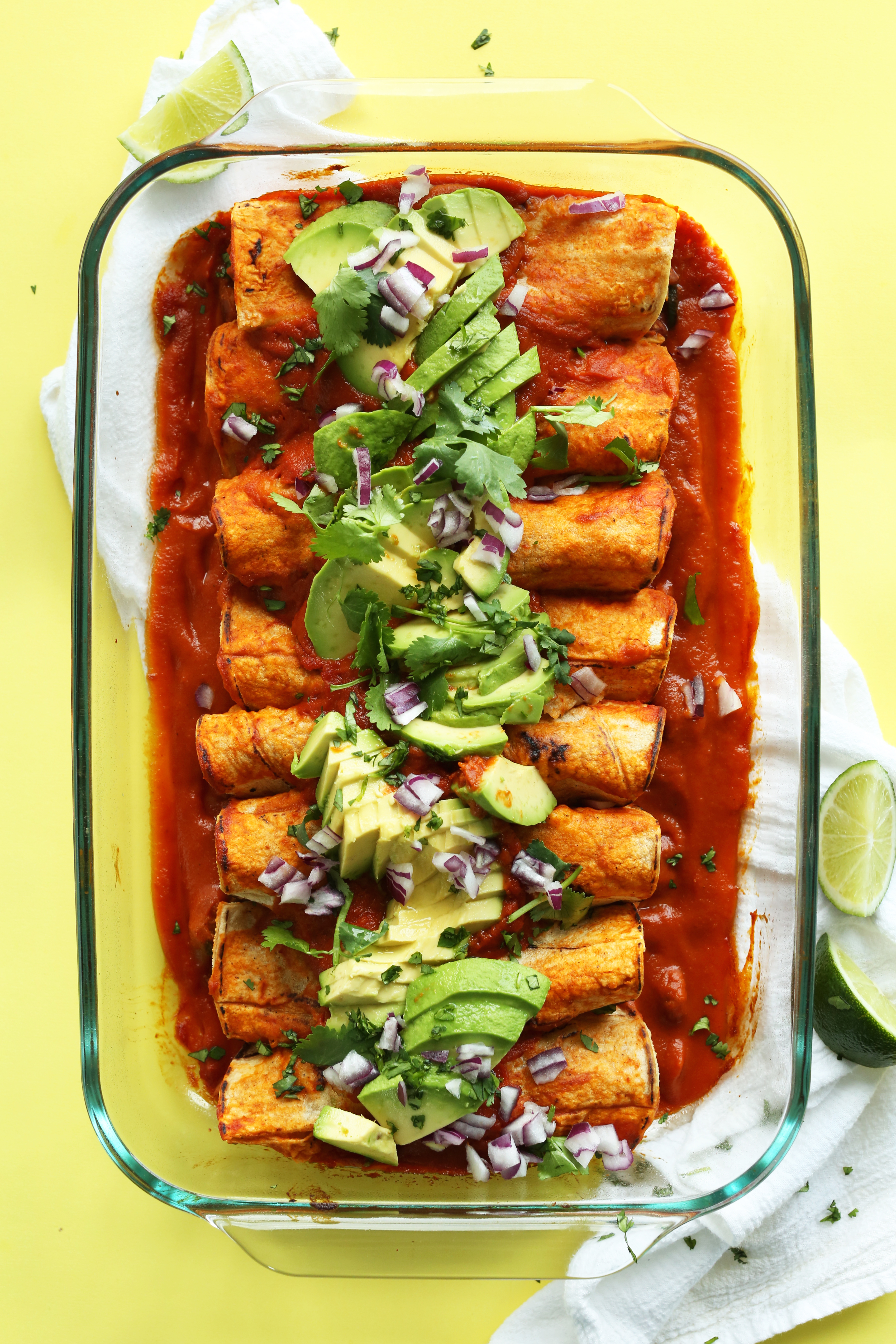 Pan of The Best Vegan Enchiladas topped with avocado, red onion, and cilantro