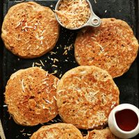 Baking sheet filled with Toasted Coconut Pancakes, syrup, and shredded coconut