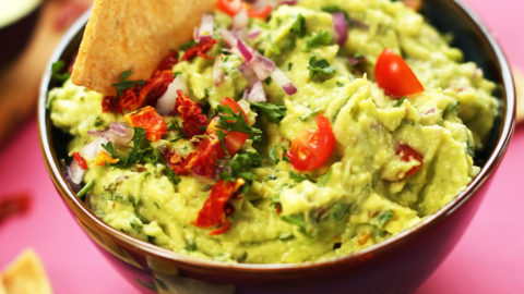 Dipping a cracker into our delicious plant-based Greek-Inspired Guacamole recipe