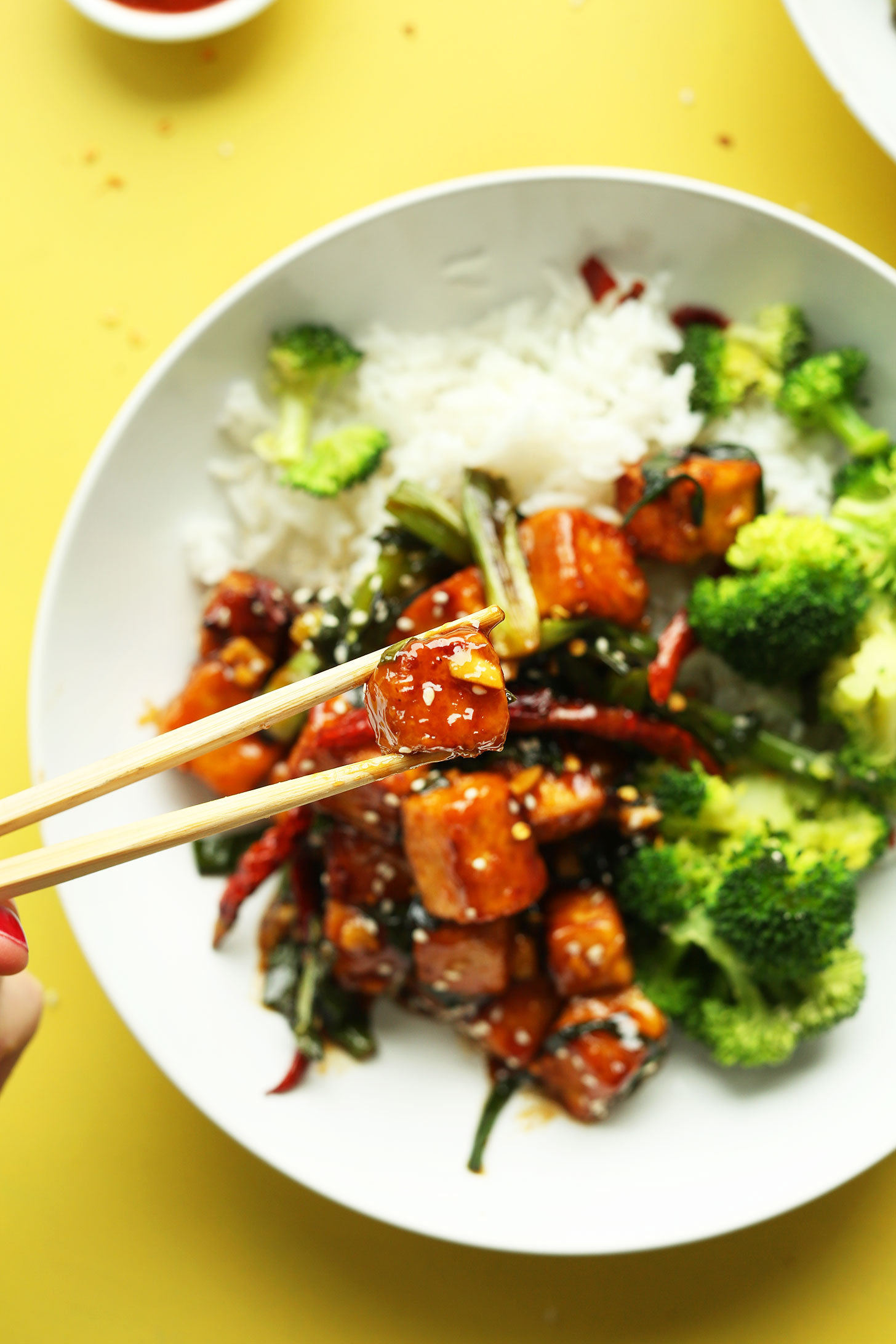 Using chopsticks to grab a bite of our General Tso's Tofu recipe for a delicious vegan dinner