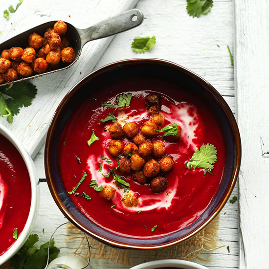 Bowl of curried beet soup with tandoori chickpeas and coriander leaves