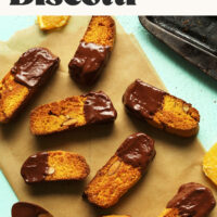 Easy vegan orange almond biscotti on a piece of parchment paper with sliced orange