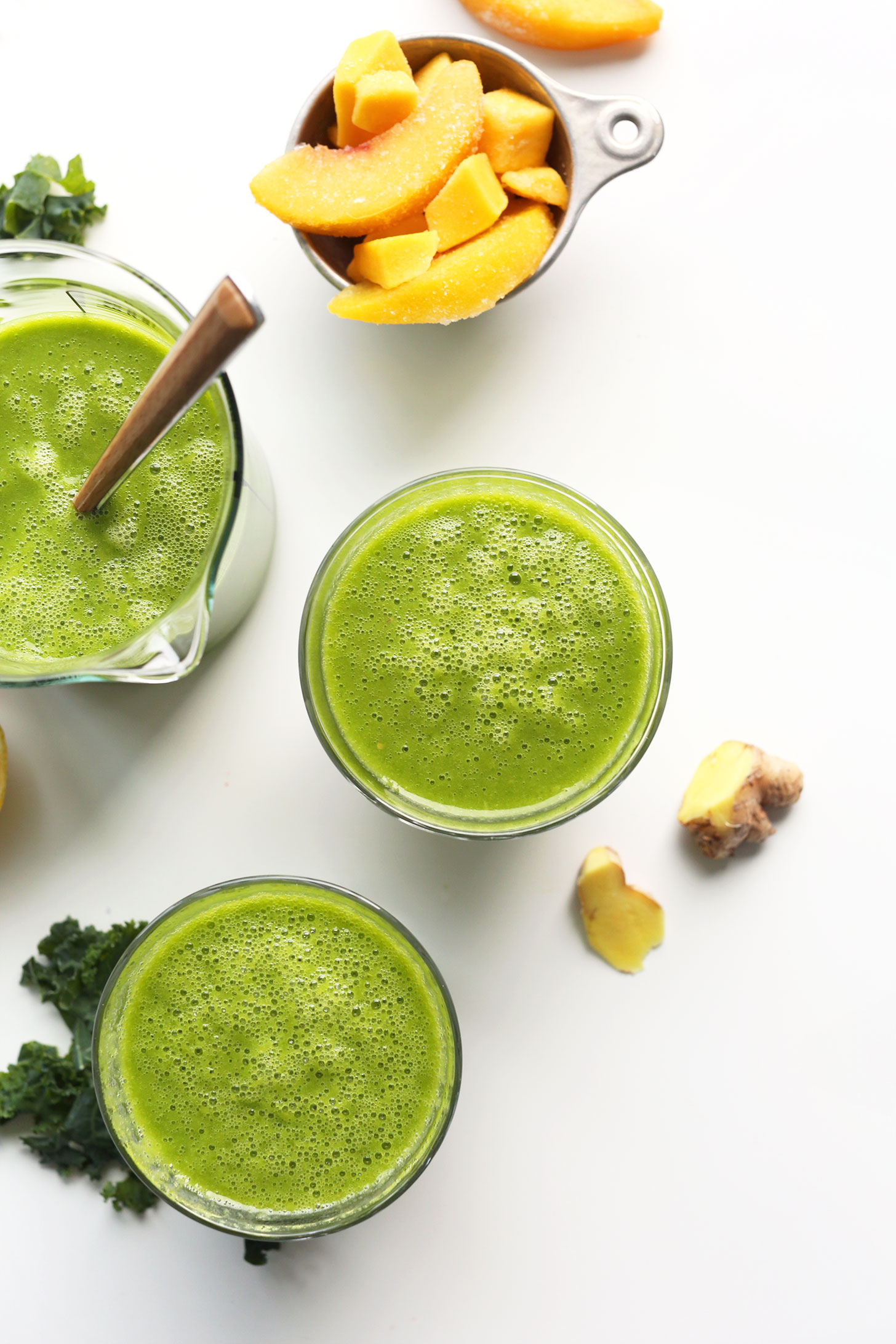Measuring glass and drinking glasses filled with our Mango Ginger Kale Green Smoothie recipe