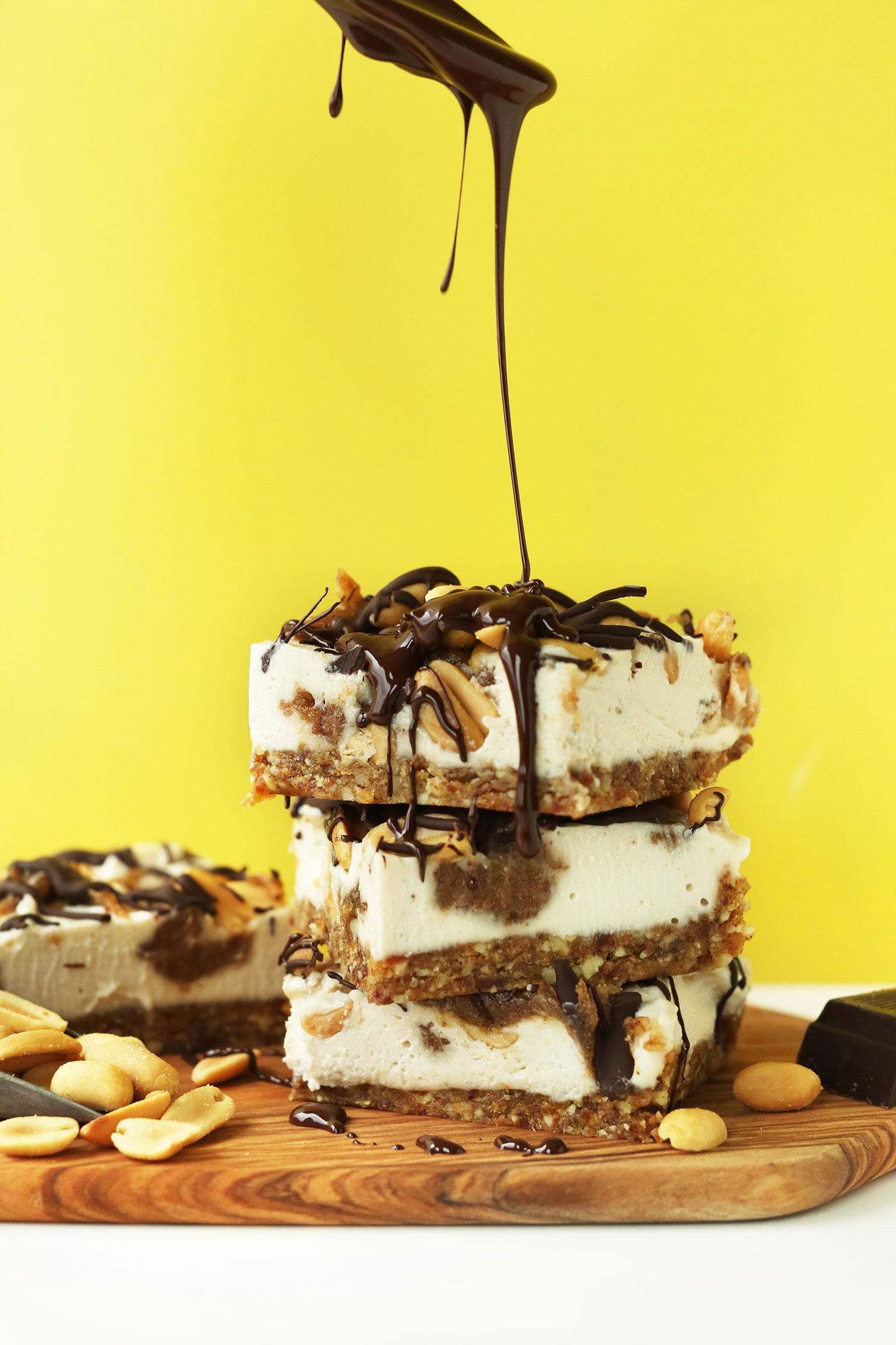 Drizzling chocolate sauce over squares of our vegan snickers cheesecake recipe