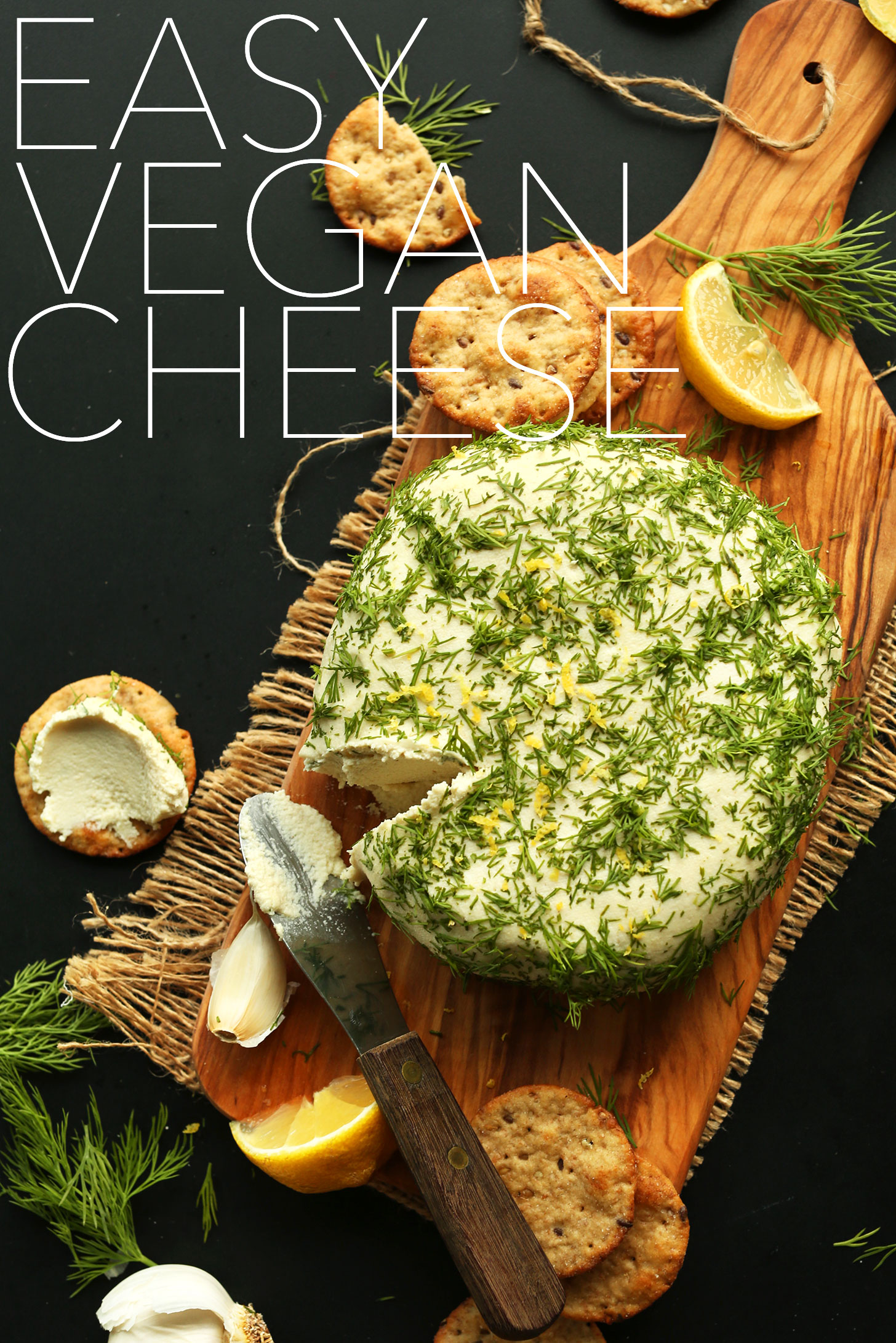 Our Easy Vegan Cheese Wheel topped with fresh dill and lemon zest on a cutting board with crackers
