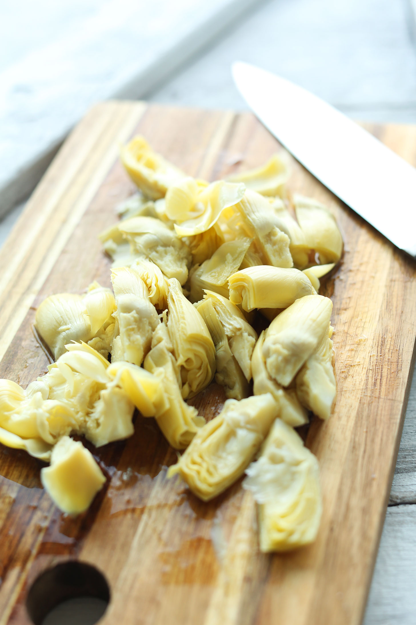 Artichoke hearts on a cutting board for making cheesy vegan artichoke dip