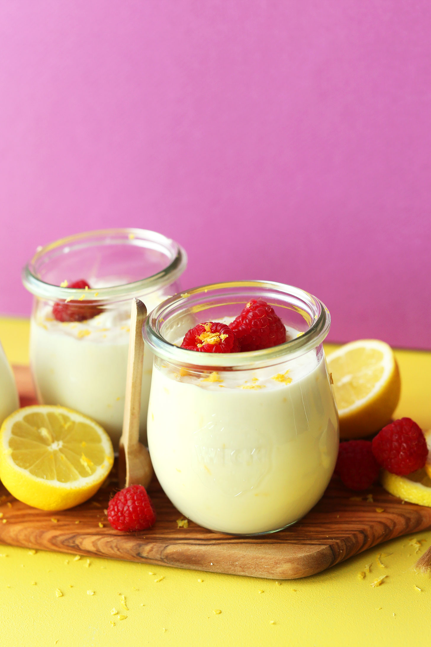 Jars of vegan lemon curd topped with fresh raspberries and lemon zest