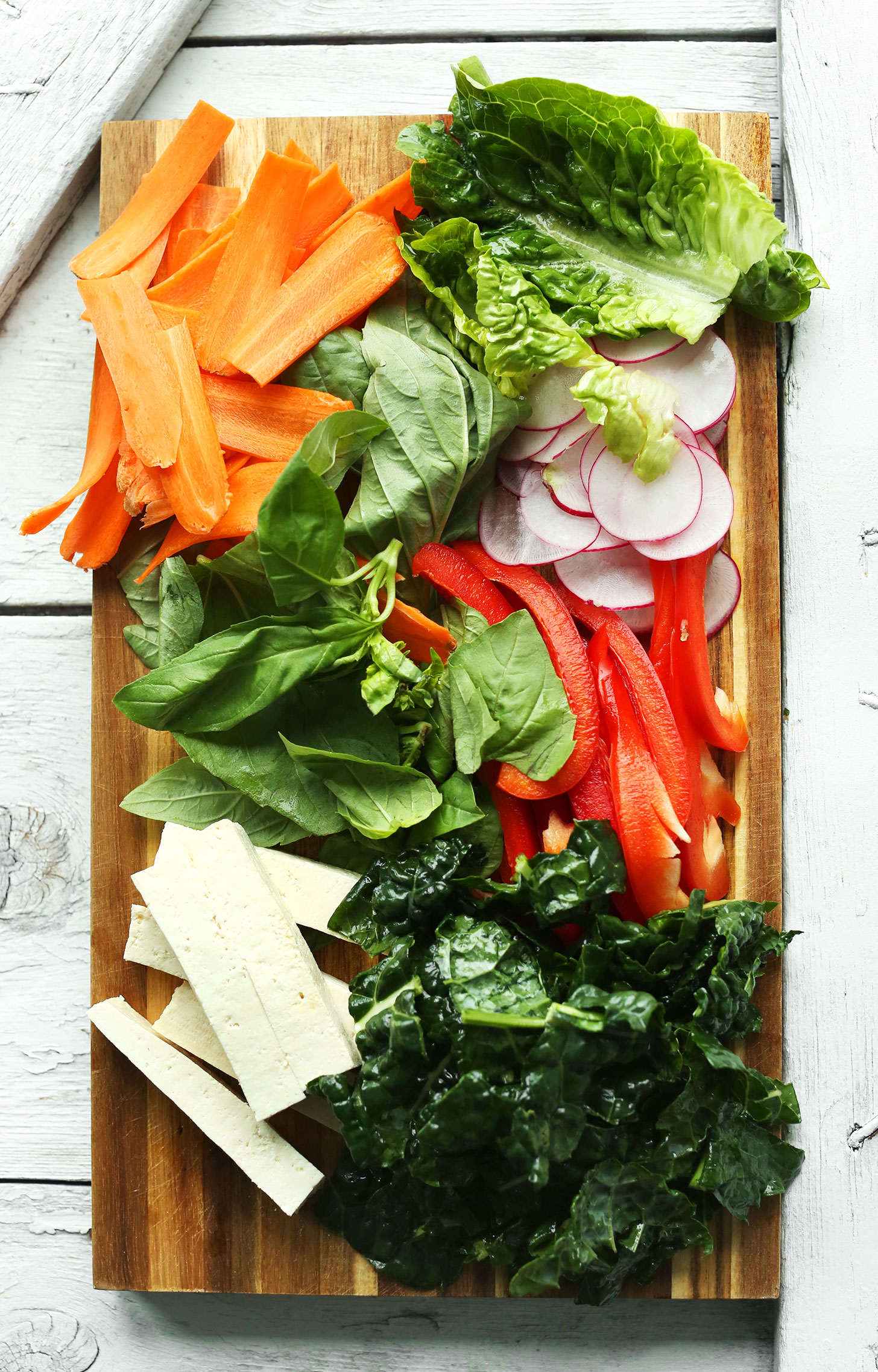 Tofu, kale, basil, bell pepper, radish, lettuce, and carrots on a cutting board