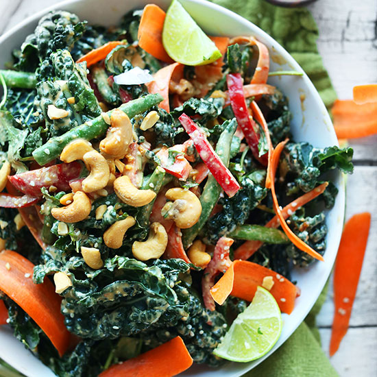 Big bowl of our amazing Gingery Thai Kale Salad topped with cashews and lime wedges