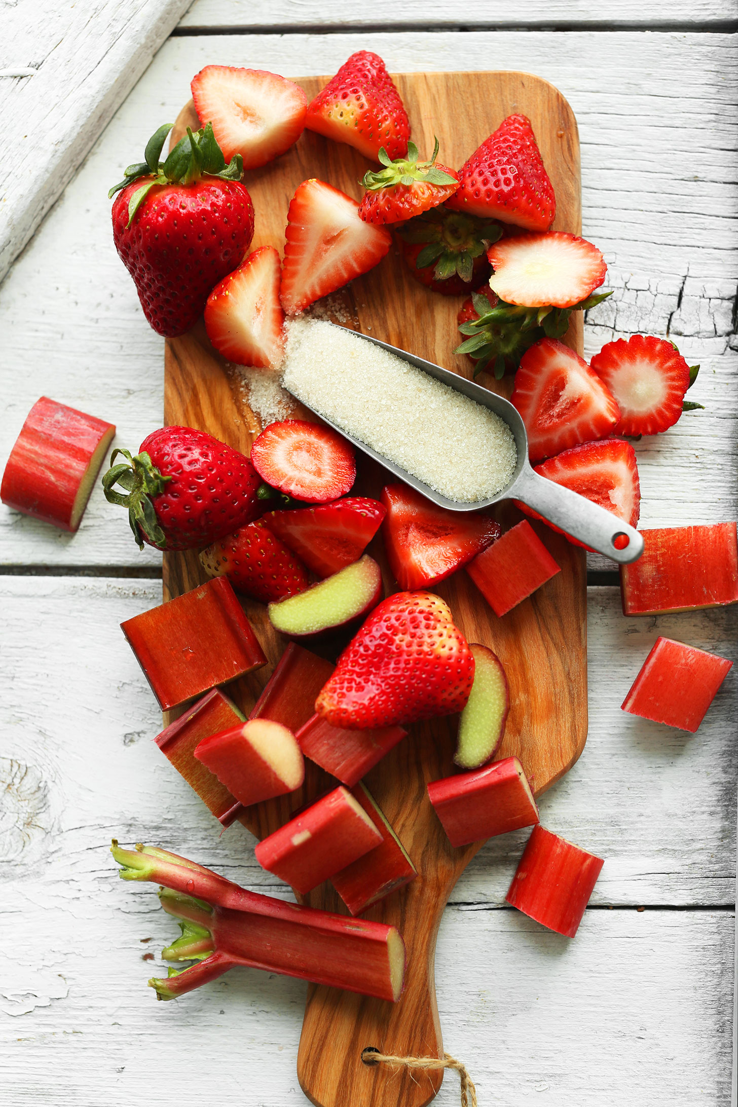 Wood cutting board with sugar, strawberries, and fresh rhubarb for making homemade strawberry rhubarb margaritas