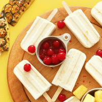 Cutting board filled with homemade Pina Colada Popsicles and cherries