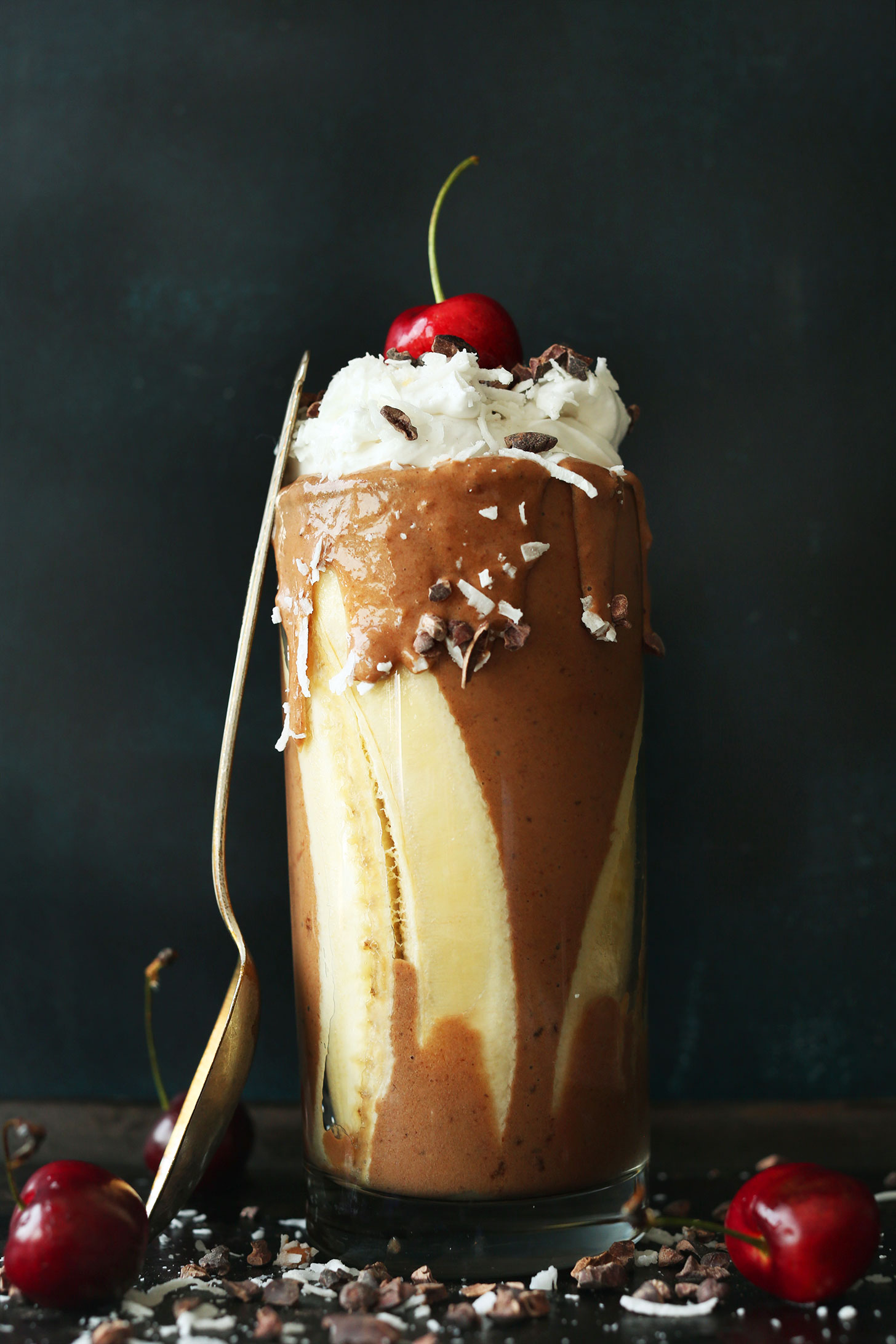 Glass of our amazing Vegan Banana Split Smoothie with Coconut Whipped Cream and a cherry on top