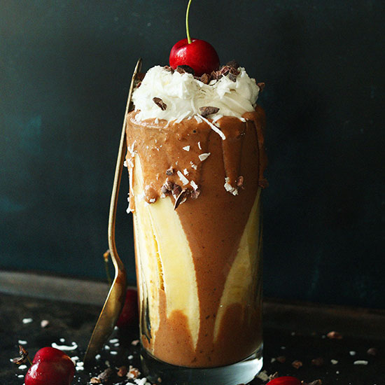 Tall mug of our Banana Split Smoothie topped with coconut whip, cacao nibs, and a cherry
