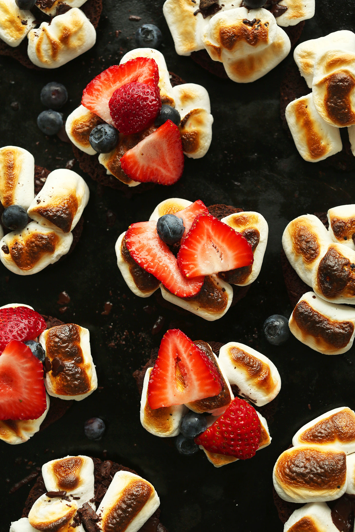 Baking sheet with gluten-free chocolate cookies topped with toasted vegan marshmallows and fresh berries