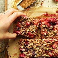 Picking up a Gluten-Free Strawberry Rhubarb Crumble Bar from a parchment-lined cutting board