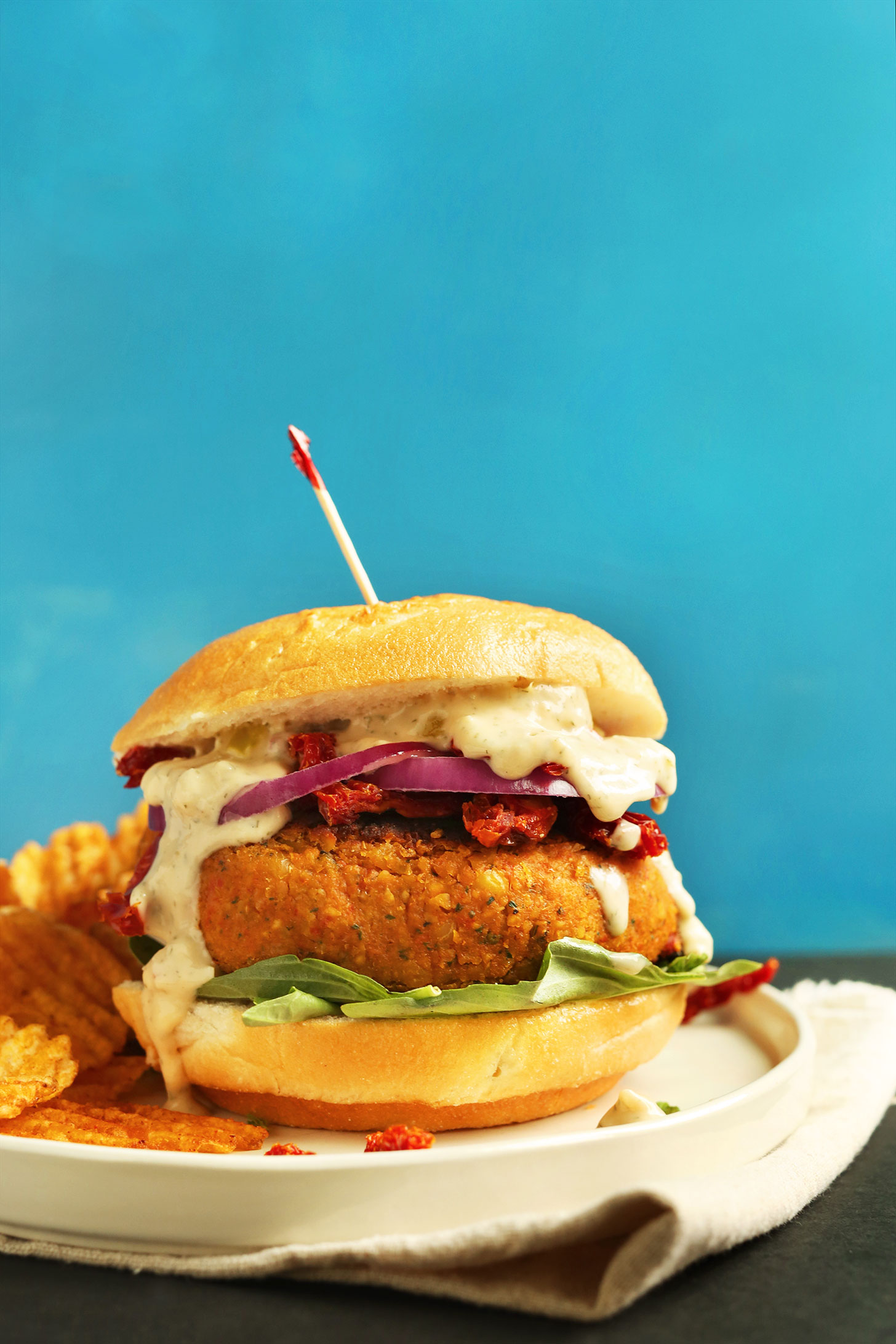 Plate of our Sun-dried Tomato Herbed Chickpea Burger recipe served with chips