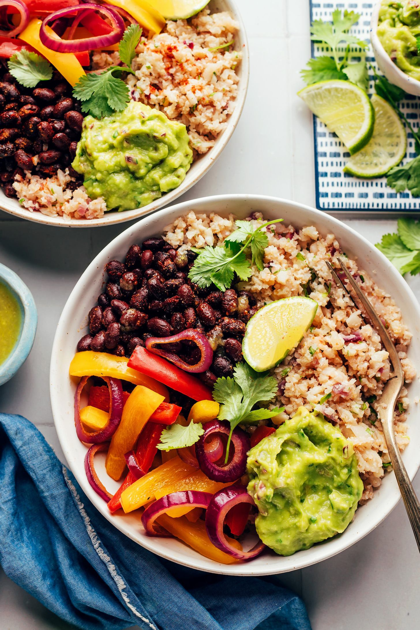 Two cauliflower rice burrito bowls with black beans, sautéd peppers and onions, and guacamole