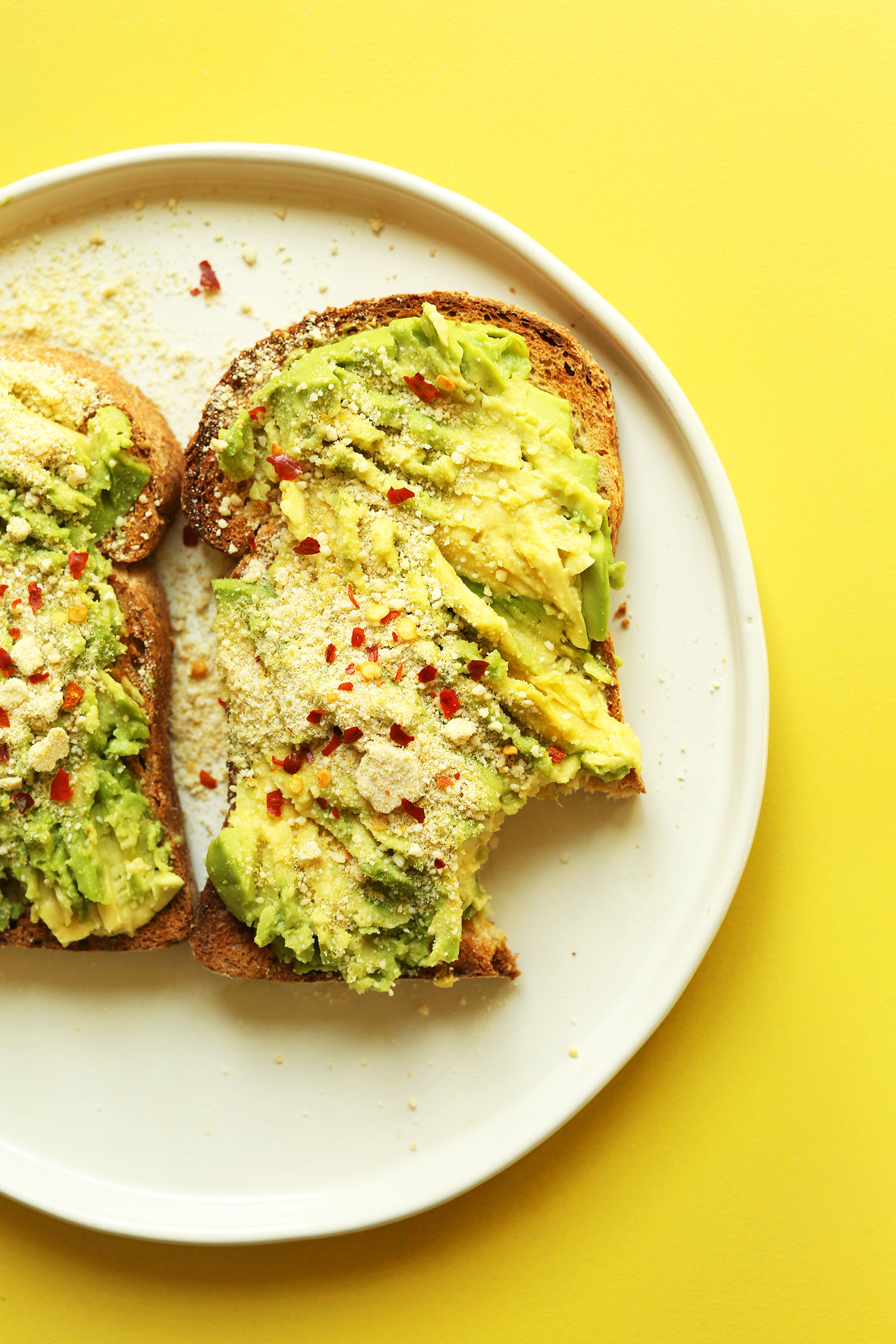 Plate of gluten-free avocado toast topped with vegan parmesan and red pepper flake