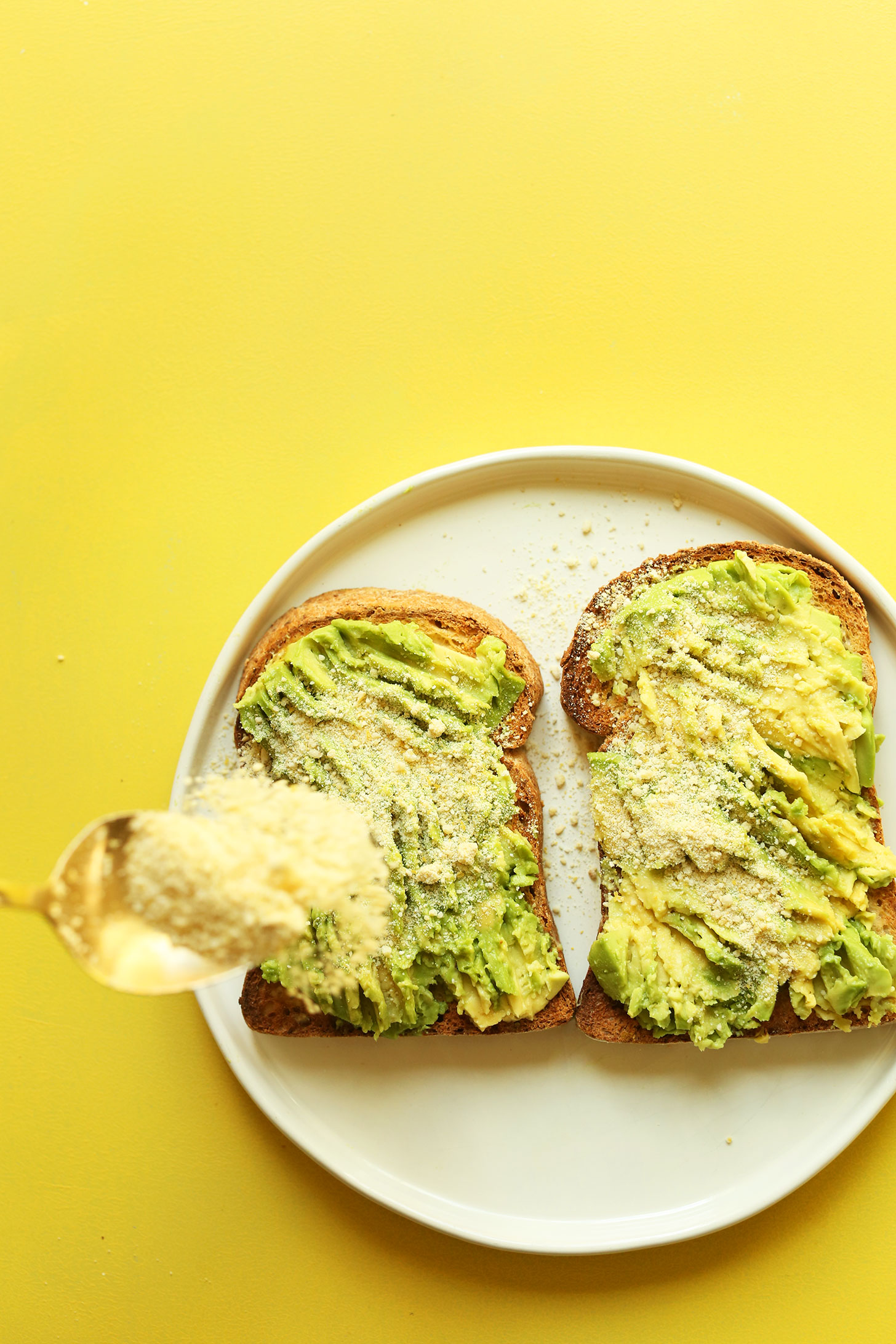 Sprinkling vegan parmesan onto avocado toast
