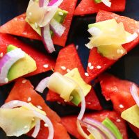 Triangular watermelon slices topped with avocado, red onion, and pickled ginger