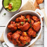 White ceramic baking dish filled with Curry Cauliflower Wings alongside a bowl of green chutney for dipping