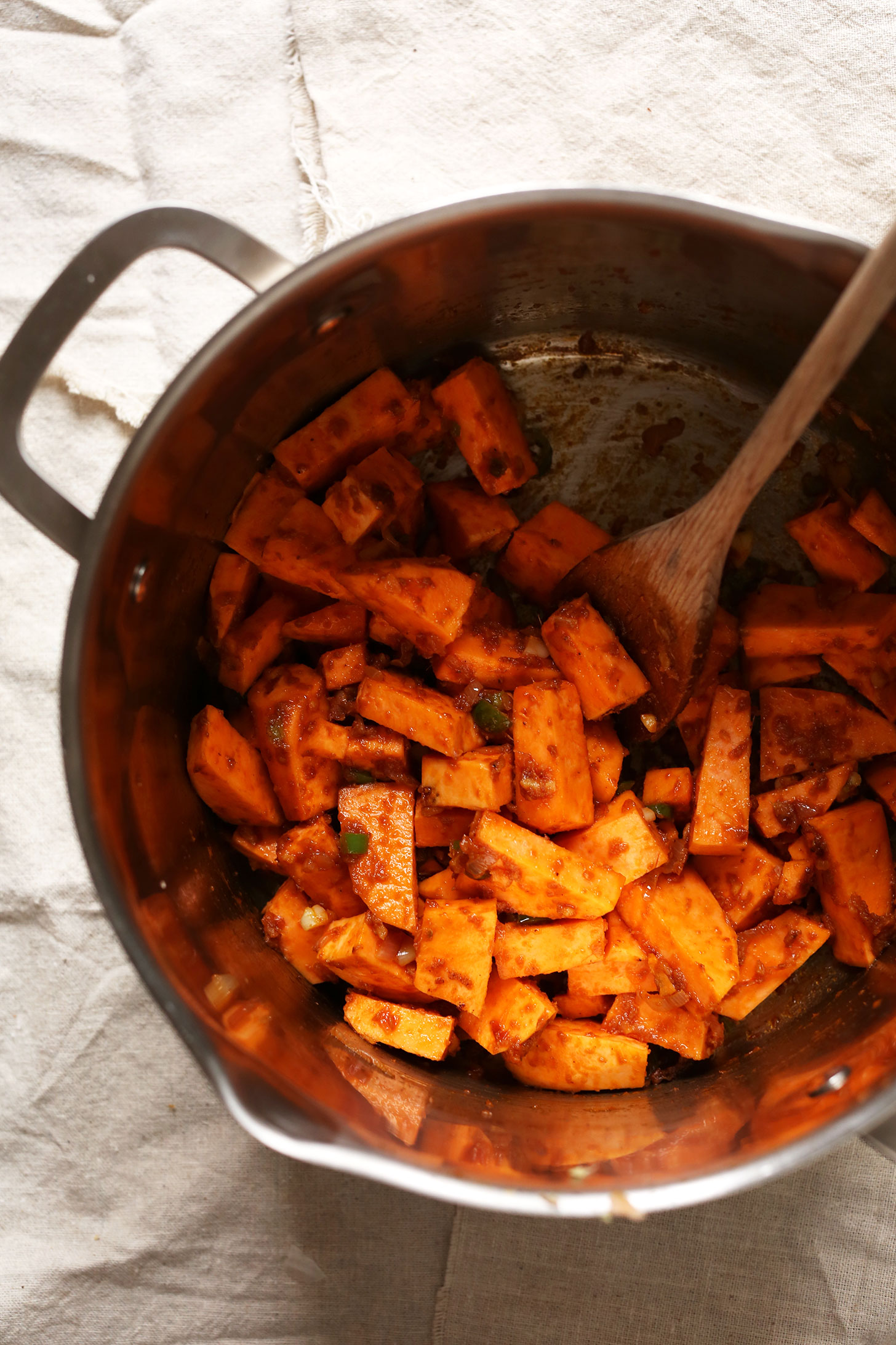 Stirring sweet potatoes and spices in a big pot for gluten-free vegan Sweet Potato Kale Curry
