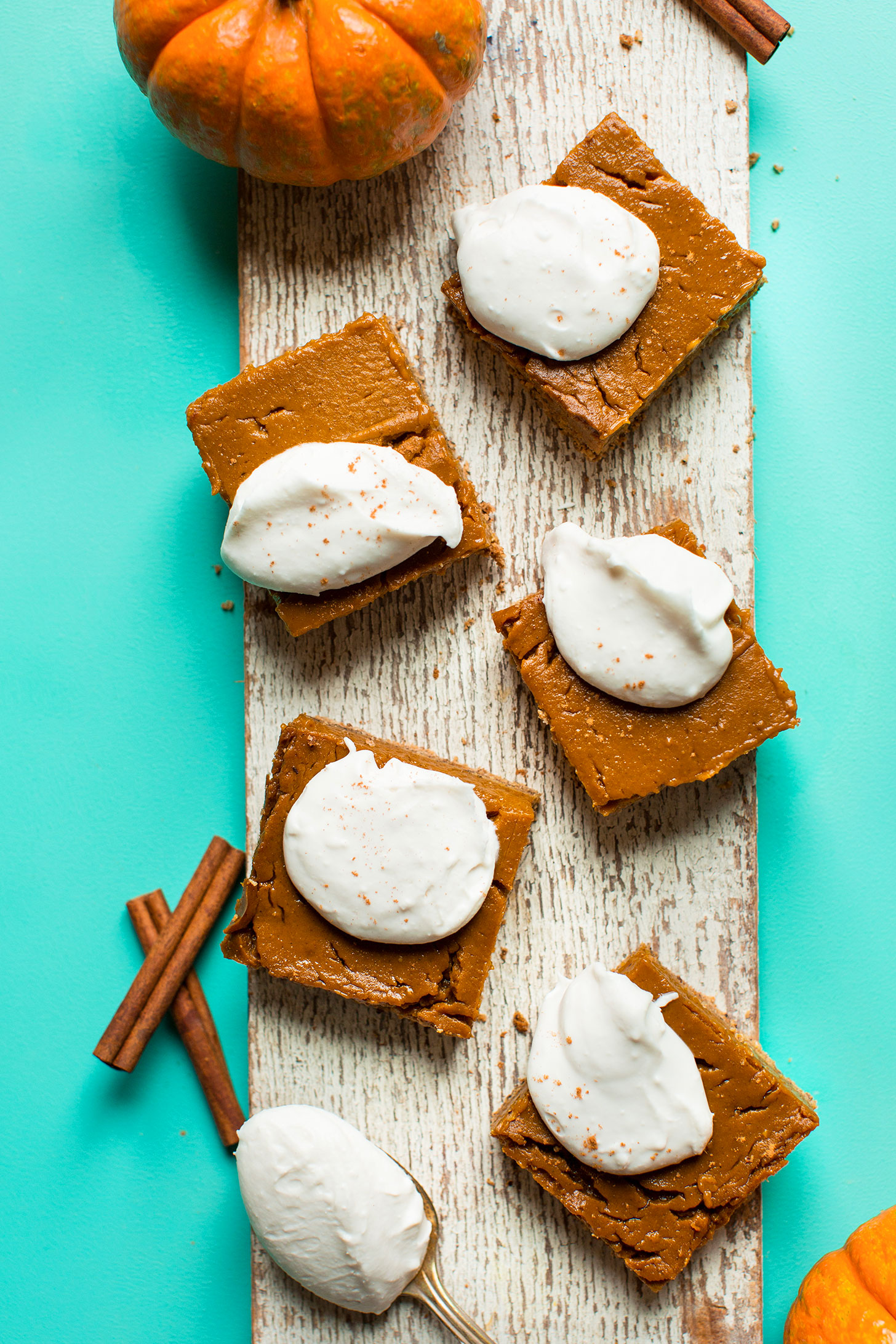 Wood plank with gluten-free vegan Pumpkin Pie Bars topped with coconut whipped cream