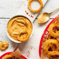 Basket of homemade Gluten-Free Onion Rings and a bowl of sauce for dipping