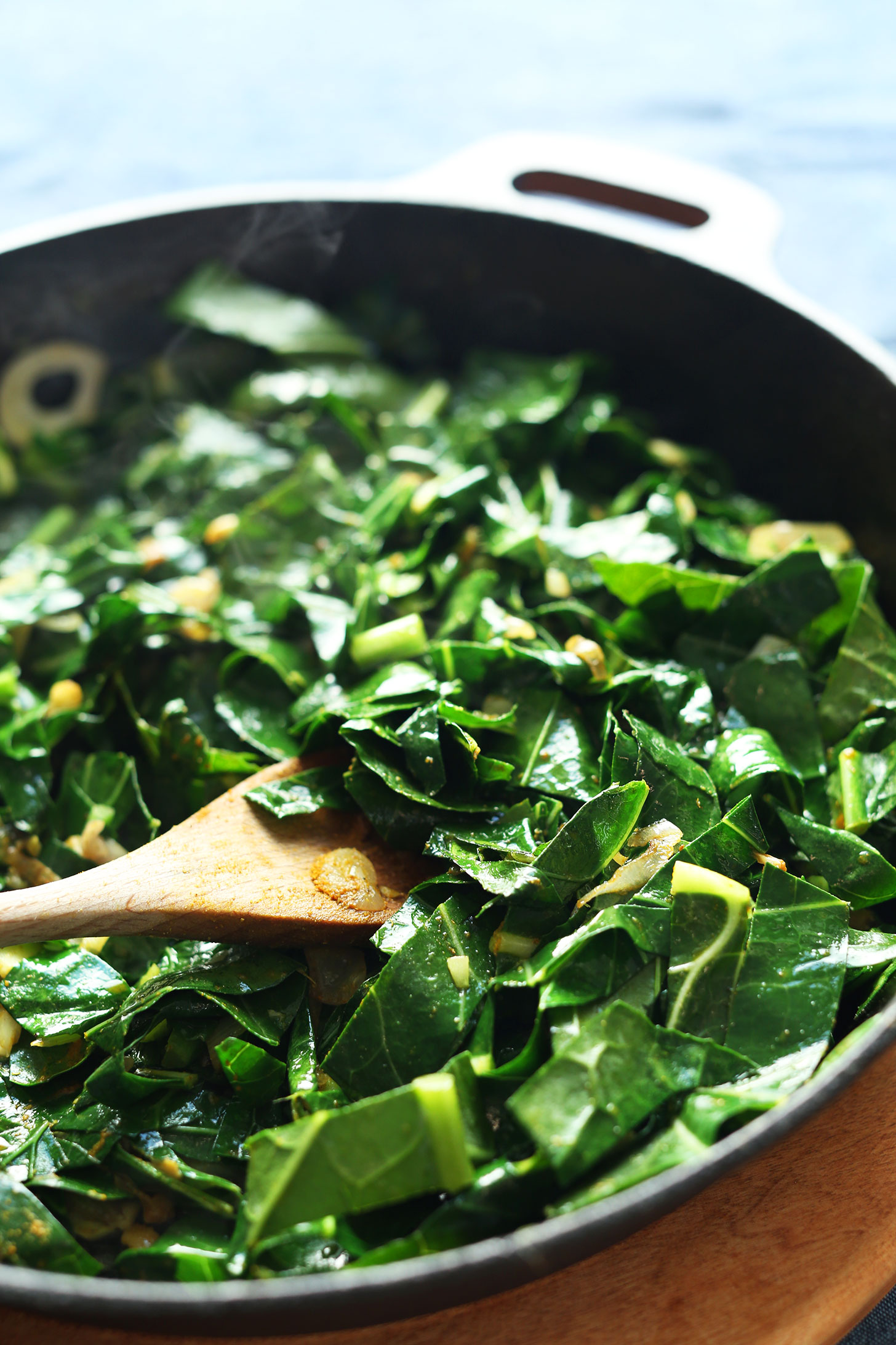 Stirring Coconut Curried Greens in a cast iron skillet for a easy, healthy, and delicious veggie dish