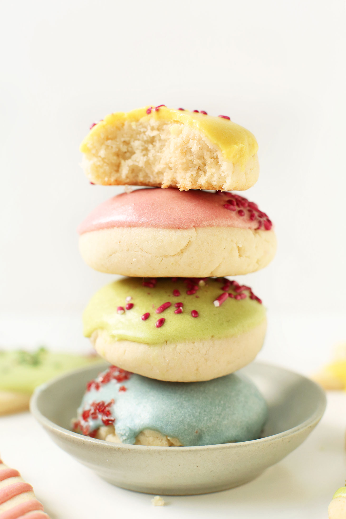 Stack of gluten-free vegan sugar cookies with yellow, pink, green, and blue frosting