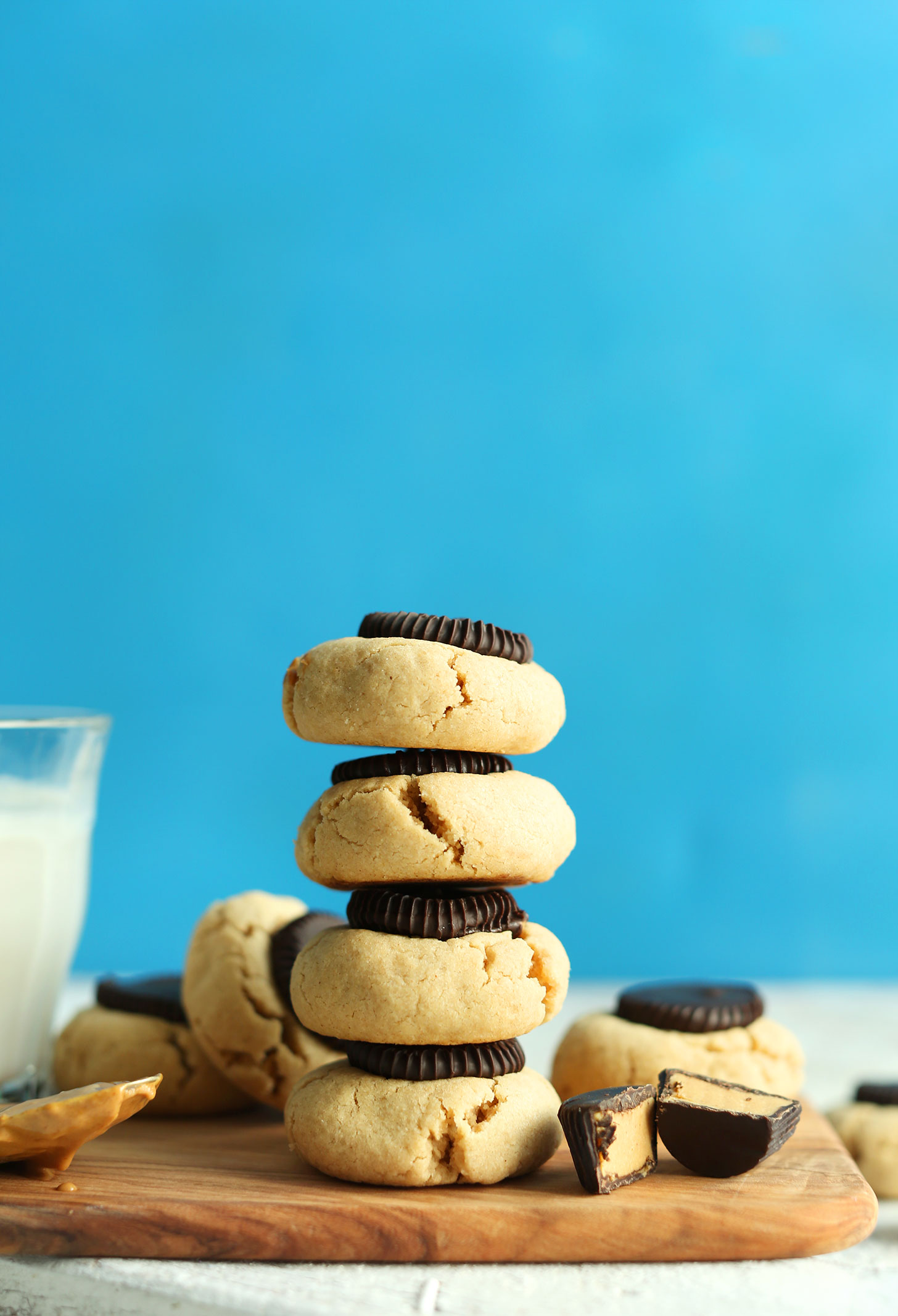 Cutting board with a glass of dairy-free milk and stack of our Peanut Butter Cup Cookies recipe
