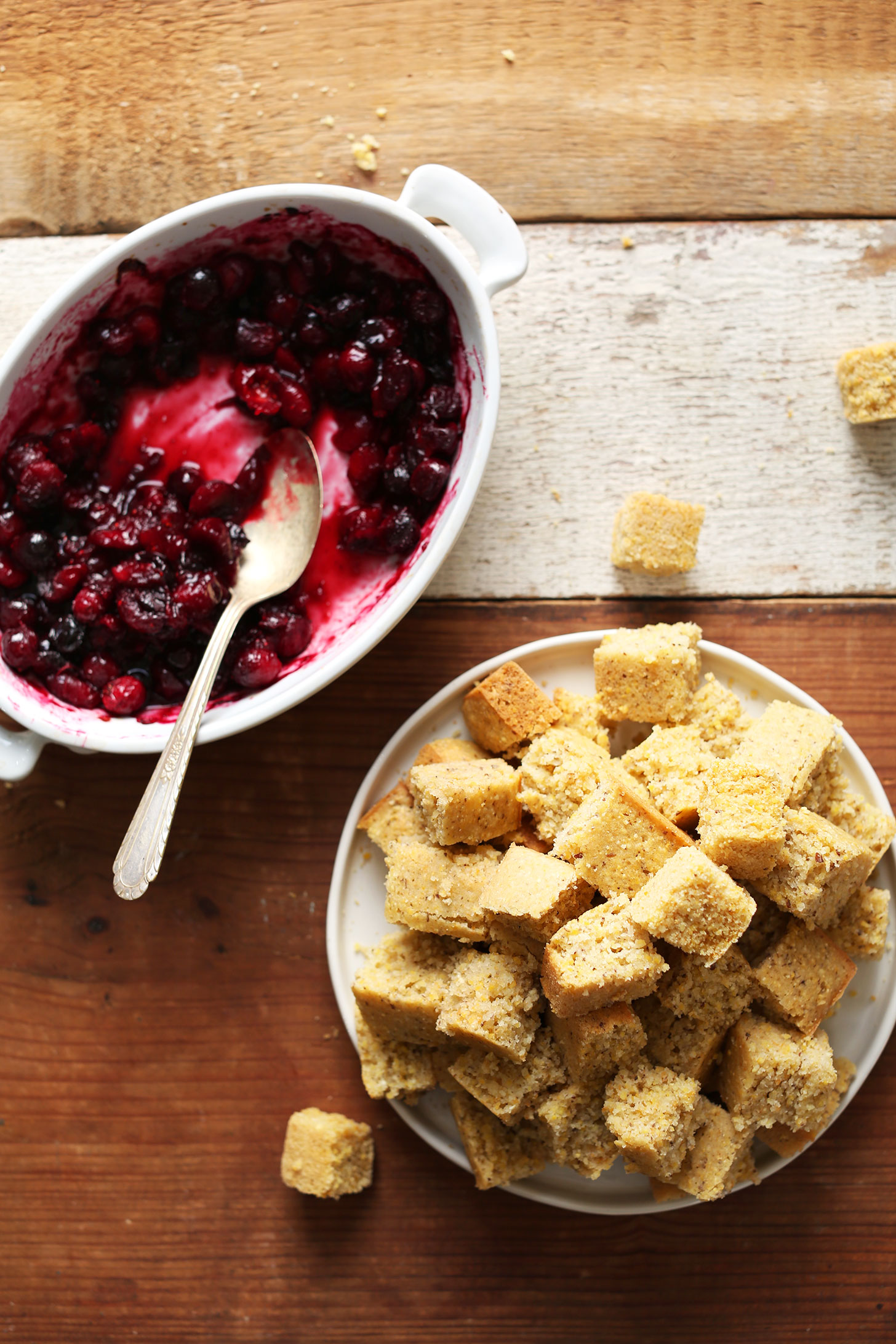 Plate of cubed vegan gluten-free cornbread and a bowl of cooked cranberries for making healthy Thanksgiving stuffing