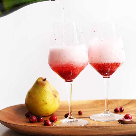 Fresh pears and cranberries on a platter with stemware filled with our Champagne Cocktails recipe