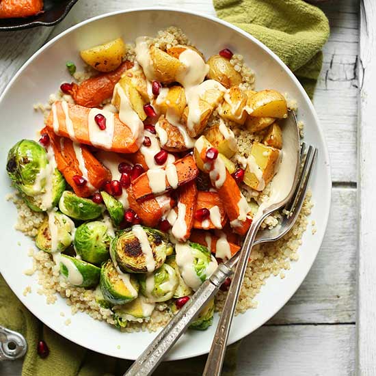 Spoon and fork in a Quinoa Harvest Bowl made with roasted vegetables and tahini sauce