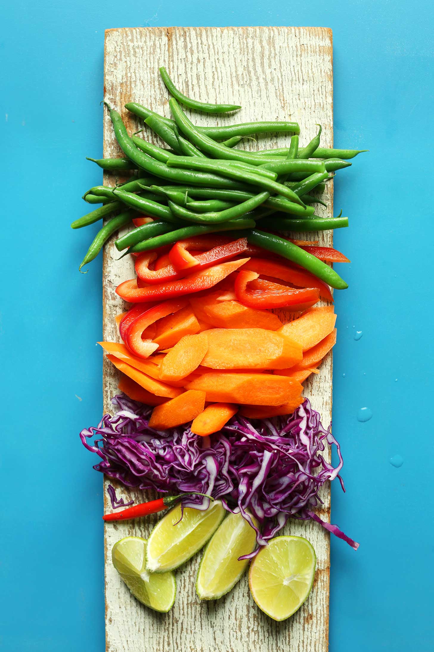 Wood plank with green beans, carrots, bell pepper, cabbage, and lime for our Quinoa Gado-Gado recipe