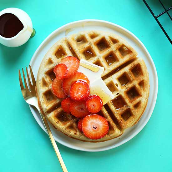 Plate with a Gluten-Free Vegan Belgian Waffle topped with sliced strawberries, vegan butter, and syrup