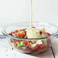 Pouring dressing into a glass bowl of our Vegan Potato Salad recipe